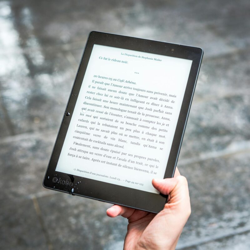 A person holds an e-reader displaying text against a wet pavement background.